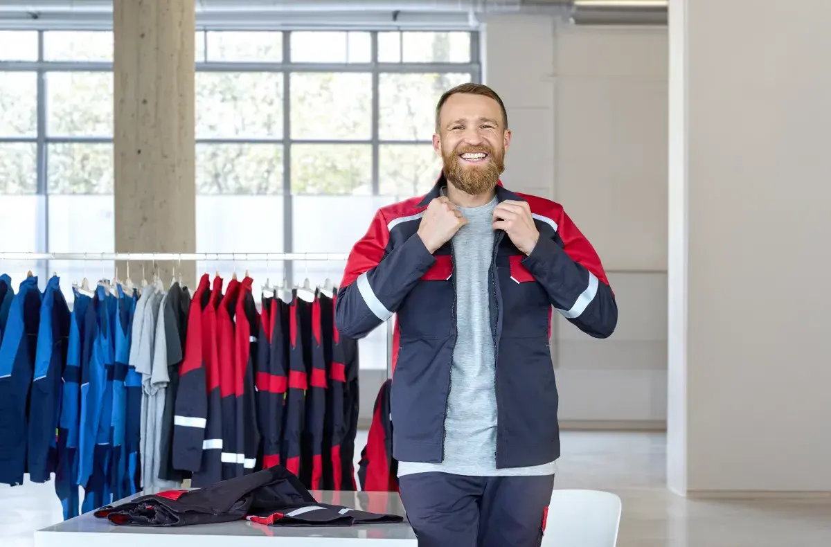 A man standing in front of the clothes rack and smiling, holding the hem of his jacket
