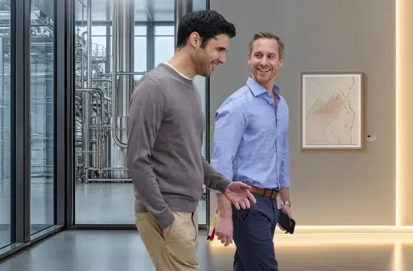 Two men pictured walking in an office building, smiling, having friendly conversation