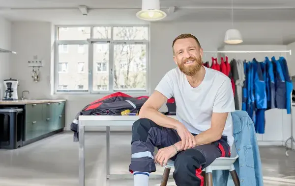 A man, seated, is taking measures of his workwear
