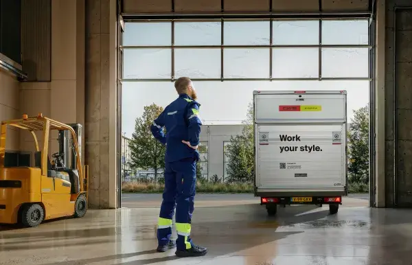 A man standing inside, facing the open door of a warehouse, CWS truck leaving