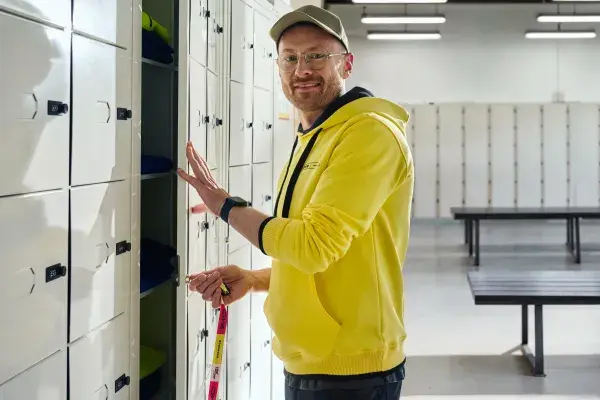 A man in a bright yellow polo is standing in front of his locker, smiling to the camera